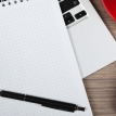 Blank notepad over laptop and coffee cup on office wooden table